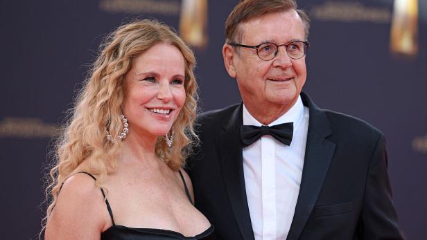 Hans Mahr mit Fliege und Moderatorin Katja Burkard mit blonden Locken lächeln auf einem Event.