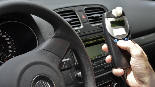 Im Cockpit eines Autos hält eine Hand ein Alkoholtestgerät.
