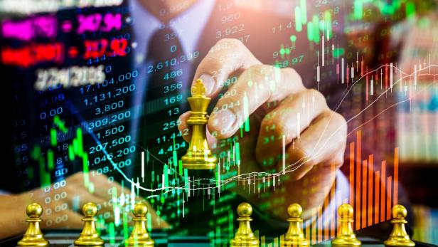 Eine Hand bewegt eine goldene Schachfigur vor einem Hintergrund mit Börsenkursen.