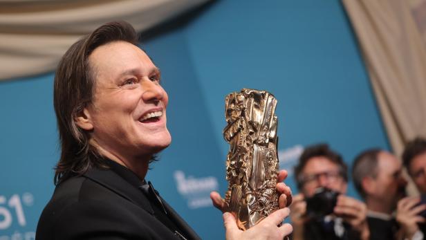 Ein lächelnder Jim Carrey bei den César Awards im Anzug hält eine goldene Trophäe in den Händen.