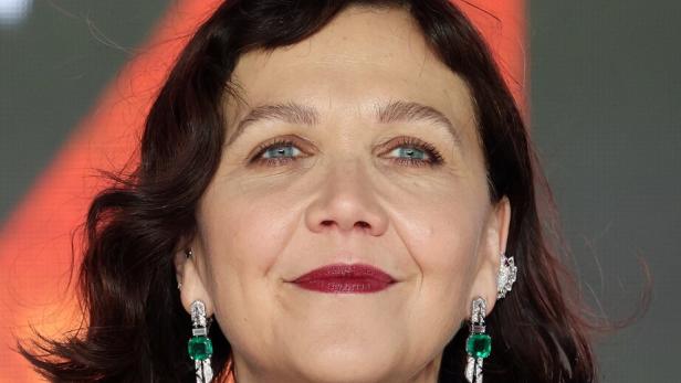 Maggie Gyllenhaal lächelt mit dunklem Lippenstift und smaragdgrünen Ohrringen.