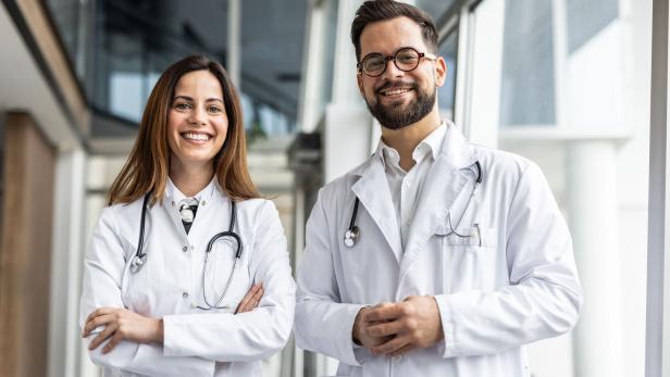 Two smiling doctors wearing white coats and stethoscopes in hospital corridor