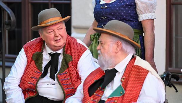 Wolfgang Schwalm and Wilfried Gliem in traditioneller Tracht unterhalten sich, eine Frau in Dirndl steht dahinter.