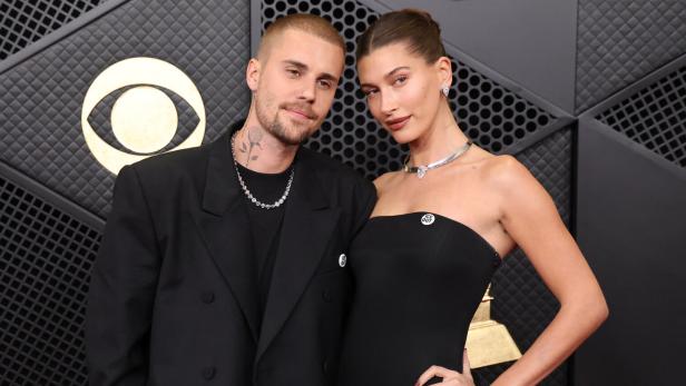 Justin und Hailey Bieber posieren in schwarzer Kleidung vor einem dunklen Hintergrund.