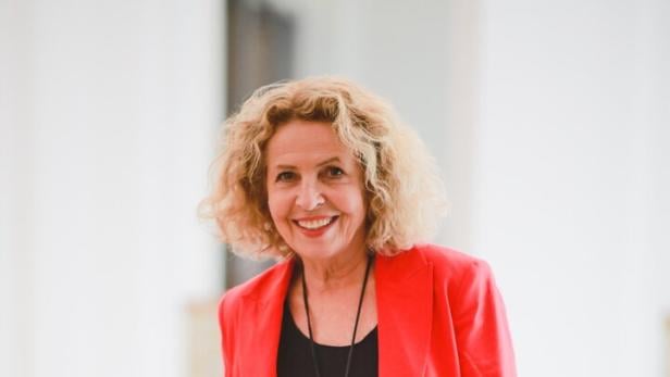 Eine lächelnde Michaela May mit blonden Locken trägt ein schwarzes Kleid und einen roten Blazer.