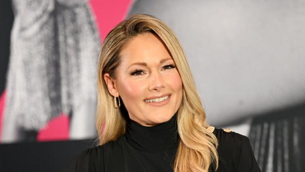 Helene Fischer lächelt mit blonden, gewellten Haaren und schwarzem Oberteil in die Kamera.