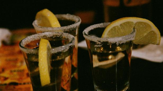 Drei Tequila-Shots mit Salzrand und Zitronenscheiben stehen auf einem Tisch in einer Bar.
