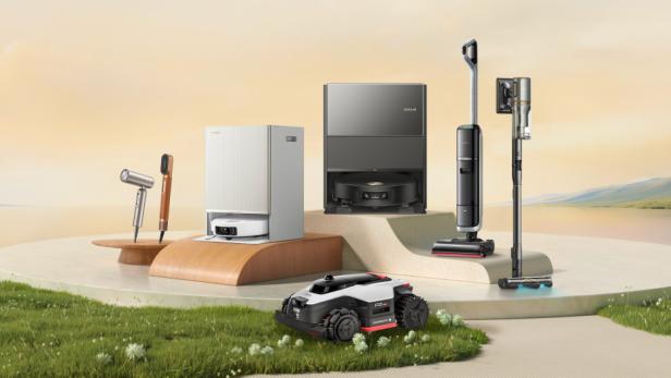 Mehrere moderne Haushaltsgeräte, darunter Staubsauger, Saugroboter, Mähroboter und ein Haartrockner, stehen auf Podesten im Freien.