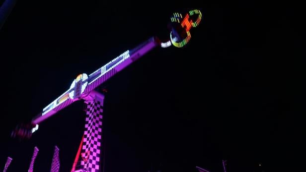 Beleuchtetes Fahrgeschäft mit rotierenden Sitzen bei Nacht auf einem Jahrmarkt.