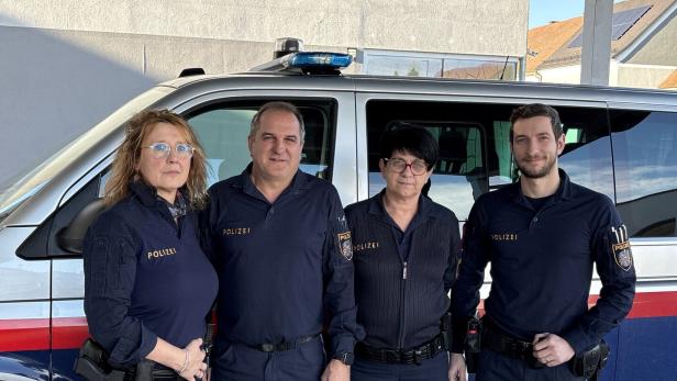 Vier Polizistinnen und Polizisten stehen in Uniform nebeneinander vor einem silbernen Polizeibus.