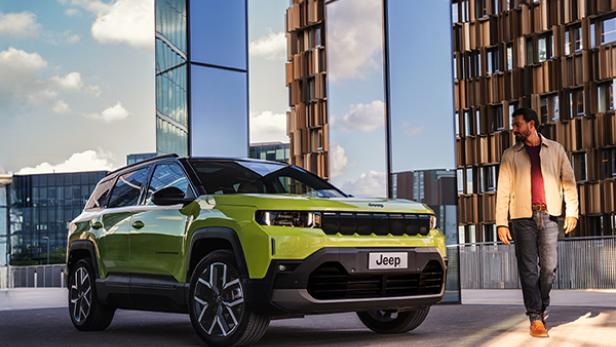 Der neue Jeep Compass steht vor einem Gebäude geparkt, daneben geht ein Mann.