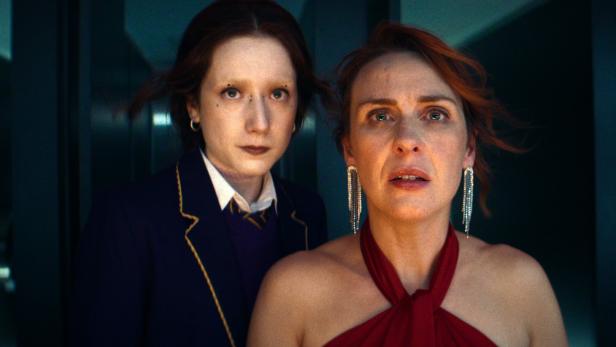 Eine Szene aus "How To Get To Heaven From Belfast": Zwei Frauen, eine im roten Kleid und die andere in Schuluniform, schauen besorgt.