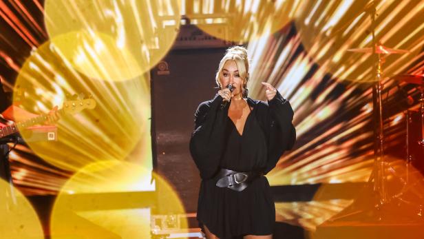 Sarah Connor performt in einem schwarzen Kleid mit Gürtel vor einem gelben Bühnenhintergrund.