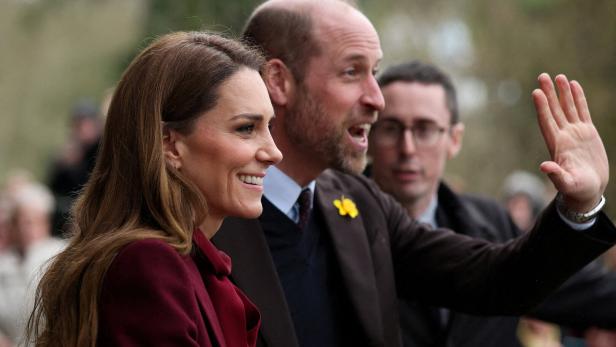 Kate und William lächeln, während William winkt und eine gelbe Blume am Revers trägt.