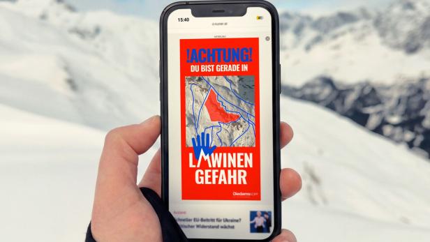Eine Hand hält ein Smartphone, das eine Lawinengefahr-Warnung für Diedamskopf anzeigt.
