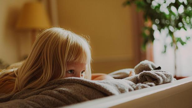 Ein blondes Mädchen liegt nachdenklich auf einem Bett und blickt zur Seite.