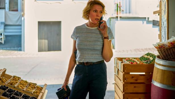 Franziska Weisz in "Mordufer" telefoniert vor einem Obststand im Freien.