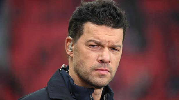 Michael Ballack mit dunklen Haaren und einem Headset im Ohr blickt ernst in die Kamera.