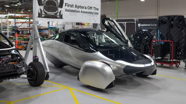 Das erste fertige Aptera-Solarauto steht mit geöffneten Türen in einer Fabrikhalle.