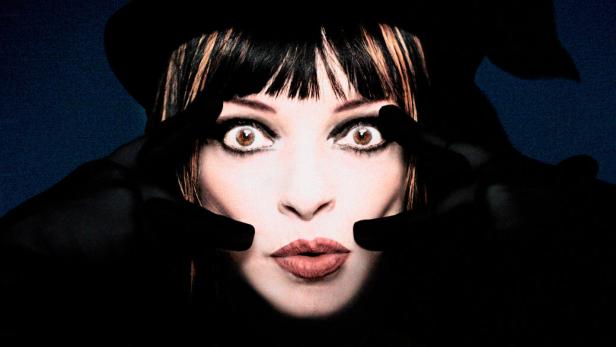 Das grell beleuchtete Gesicht der Musikerin Nina Hagen, die aus der Dunkelheit mit aufgerissenen Augen in die Kamera blickt