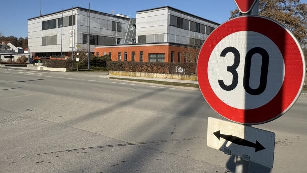 Ein 30 km/h-Schild steht am Straßenrand vor einem modernen Bürogebäude.