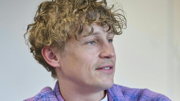 Tim Bendzko mit blonden Locken und lila Hemd blickt zur Seite.