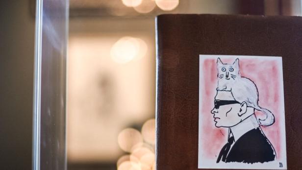 Ein Bild zeigt eine Zeichnung von Karl Lagerfeld mit seiner Katze Choupette auf dem Kopf.