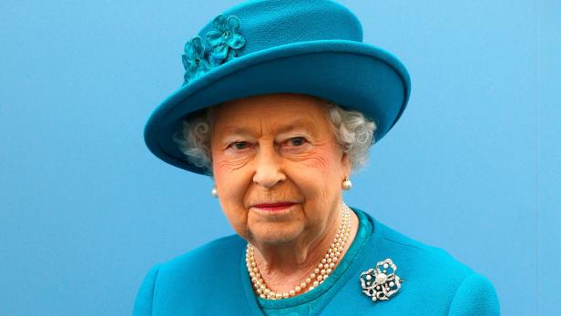 Königin Elisabeth II. trägt einen türkisfarbenen Hut mit Blumen und eine Perlenkette.