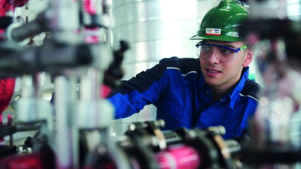 Ein Arbeiter mit Schutzhelm und Brille inspiziert eine industrielle Anlage.