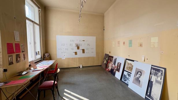 Ein spärlich eingerichteter Raum mit alten Fotografien, Dokumenten und Tafeln an den Wänden sowie Tischen und Stühlen.