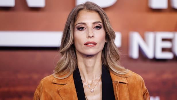 Cathy Hummels mit blonden Haaren und brauner Jacke mit Fransen blickt in die Kamera.