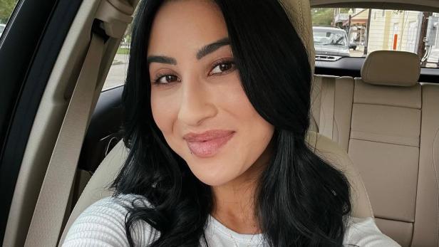 Frau mit langen dunklen Haaren lächelt auf dem Beifahrersitz eines Autos in die Kamera.