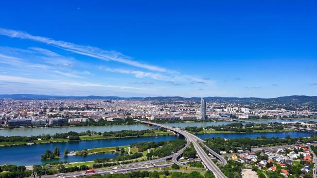 Die Donau schlängelt sich durch Wien, überbrückt von Autobahnen und mit dem DC Tower im Hintergrund.