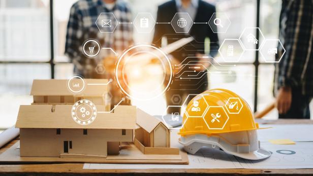 Ein gelber Bauhelm und ein Architekturmodell stehen auf einem Tisch, im Hintergrund sind unscharfe Personen und digitale Symbole zu sehen.