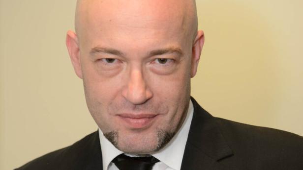 Der Graf mit Glatze und im schwarzen Anzug mit weißem Hemd und schwarzer Krawatte schaut direkt nach vorn.