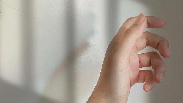 Hand mit kurzen, gepflegten Fingernägeln vor neutralem Hintergrund im Sonnenlicht.