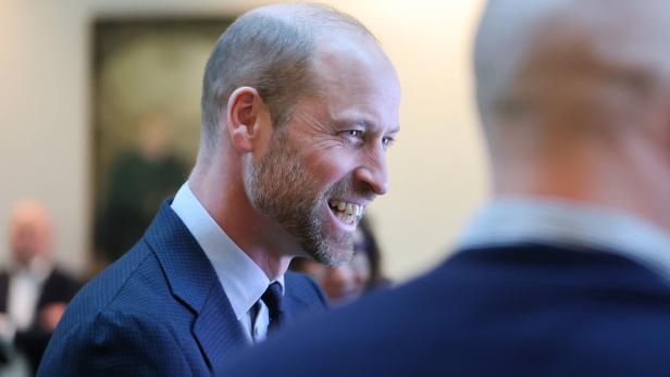 Prinz William lächelt in einem dunklen Anzug, während er sich mit jemandem unterhält.