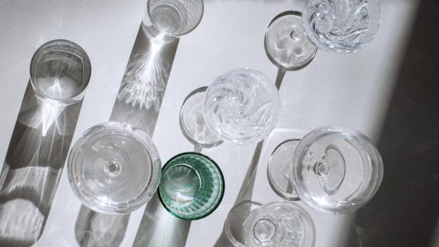 Mehrere leere Glasgefäße werfen Lichtreflexe und Schatten auf eine helle Oberfläche.