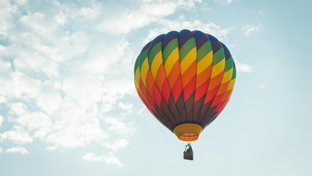 Heißluftballon mit buntem Muster schwebt vor blauem Himmel mit Wolken.