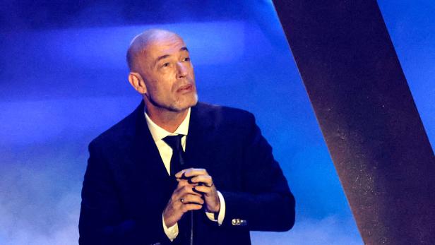 Der Graf von Unheilig steht im Anzug auf der Bühne und blickt nachdenklich nach oben, während er ein Mikrofon hält.