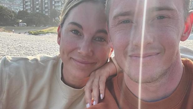 Pärchen sitzt am Strand und lächelt in die Kamera