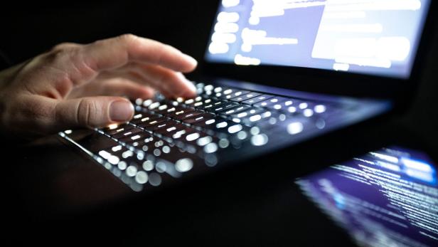 Eine Hand tippt auf einer beleuchteten Tastatur eines Laptops mit unscharfem Bildschirm im Hintergrund.