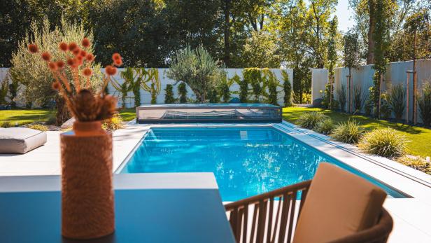 Ein Tisch auf einer Terrasse mit einer Vase und Blumen, im Hintergrund sieht man einen Garten mit Swimmingpool.