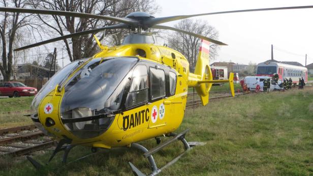 Ein gelber Rettungshubschrauber des ÖAMTC steht neben einem Unfall mit einem Zug.