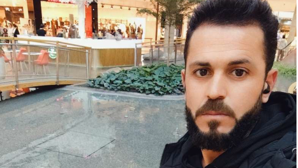 Ein Selfie des Vaters mit Kopfhörer im Ohr und dichtem dunklen Bart vor einem Geschäft.