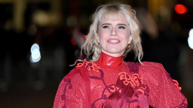 Paloma Faith mit blonden Haaren lächelt in einem roten Kleid mit hohem Kragen.