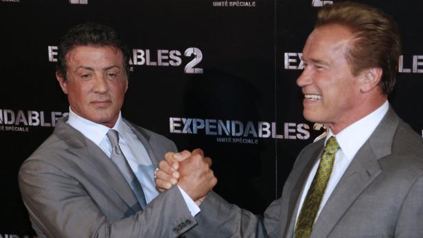 Sylvester Stallone und Arnold Schwarzenegger geben sich vor "Expendables 2"-Logo die Hand.