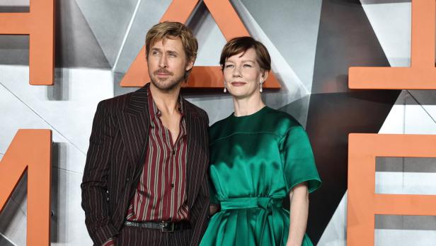 Ryan Gosling im Anzug und Sandra Hüller in einem grünen Kleid posieren vor einem geometrischen Hintergrund.