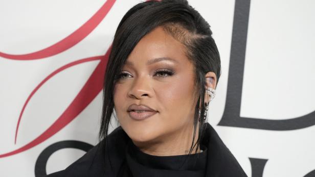 Rihanna mit dunklem Haar und auffälligem Ohrschmuck vor einem gemusterten Hintergrund.