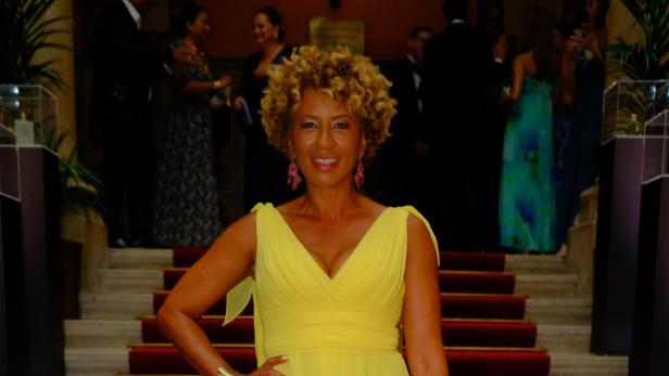 Arabella Kiesbauer in einem gelben Kleid auf einer Treppe